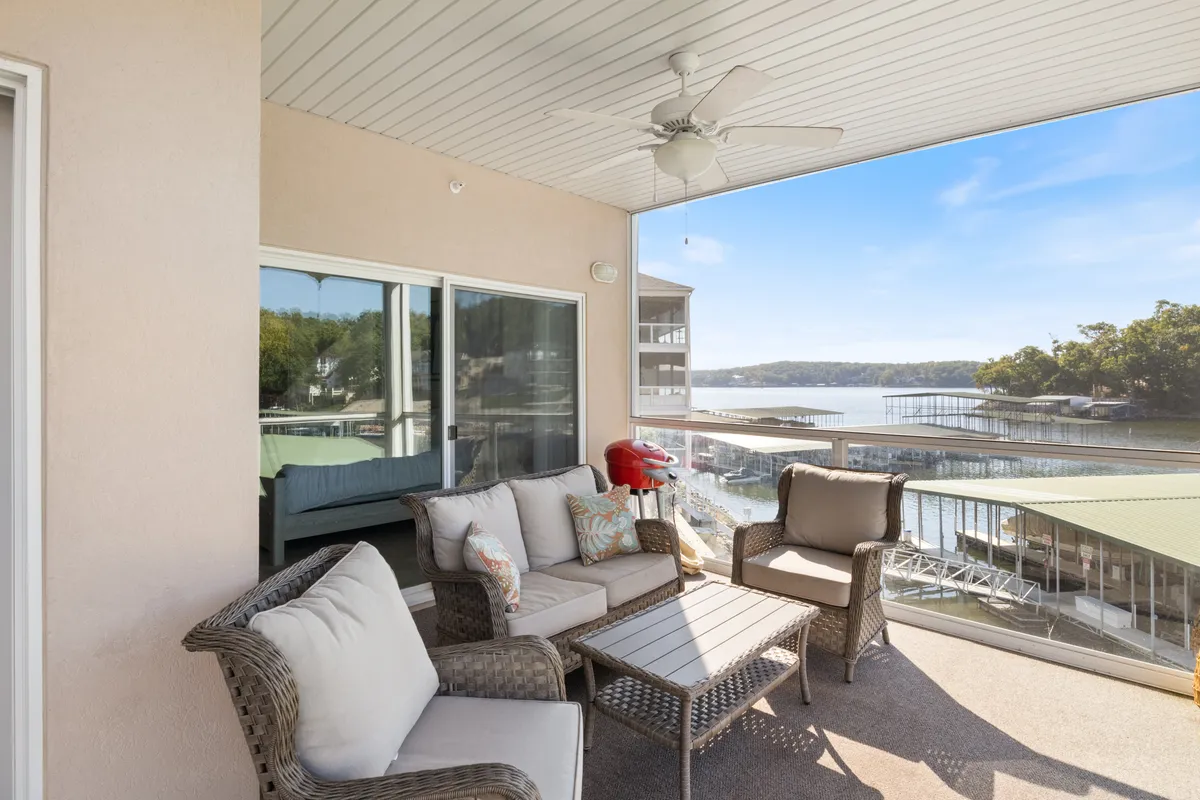 A screened-in deck furnished with comfortable seating and a ceiling fan, overlooking calm lake waters. The setting is serene, perfect for sipping coffee, enjoying alfresco meals, or taking in stunning sunsets over the cove.