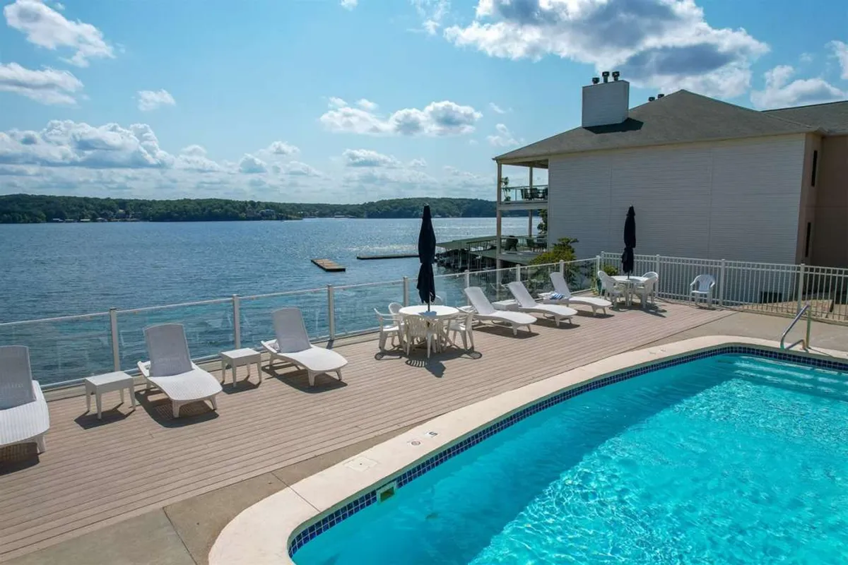 This serene exterior image showcases a beautiful swimming pool surrounded by comfortable lounge chairs, with a sweeping view of the lake and a spacious patio area. The tranquil mood is enhanced by the natural light reflecting off the water and the inviting setup for sunbathing or social gatherings.