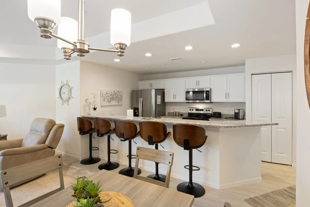 A warm, inviting kitchen space is visible, with a central island surrounded by bar stools, contemporary light fixtures overhead, and a dining table set nearby. The open design encourages both cooking and socializing, making it ideal for group activities.