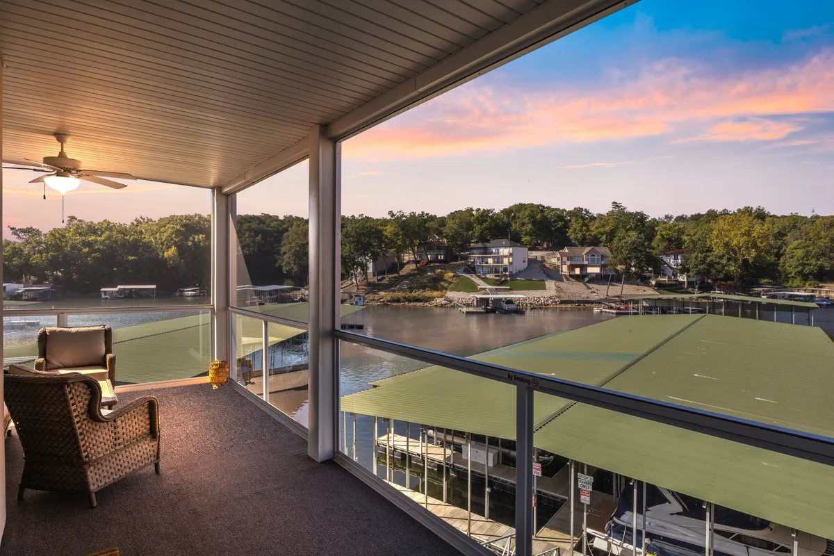The hero image showcases the condo's private balcony with comfortable seating, overlooking a tranquil marina. The sun is setting, bathing the scene in warm, golden hues. Boats are docked nearby, and the water reflects the colorful sky, creating a peaceful, inviting atmosphere that hints at relaxation and outdoor enjoyment.