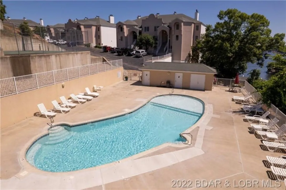 This image features a sparkling swimming pool surrounded by lounge chairs and nearby residential buildings. The relaxed scene suggests opportunities for sunbathing, swimming, and group socializing, with hints of a sunset ambiance that enhances the vacation mood.