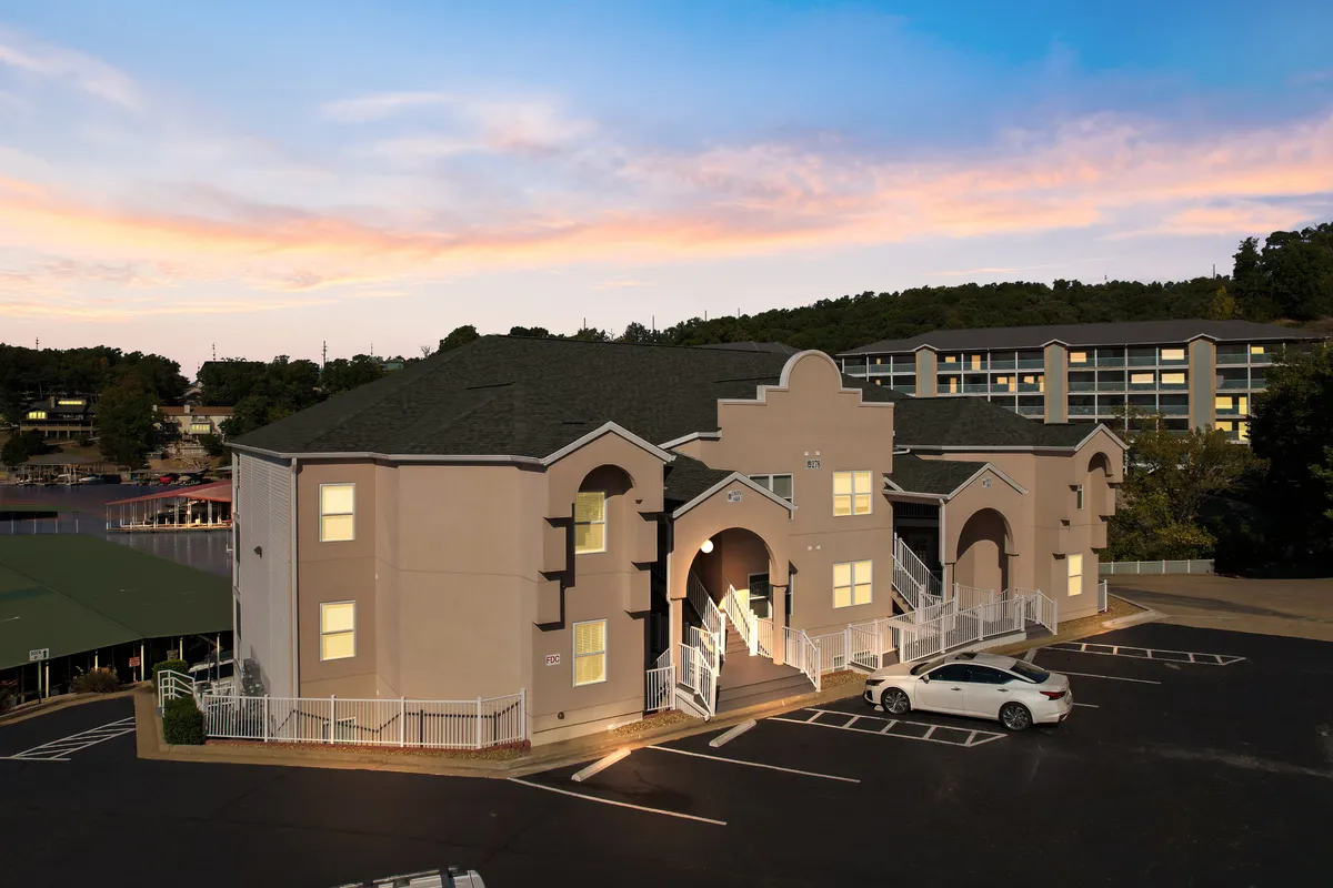 This photo highlights the welcoming front entrance of the building, complete with a few steps, surrounding greenery, and cars parked nearby. The tranquil, inviting exterior sets the tone for easy access and a sense of community.