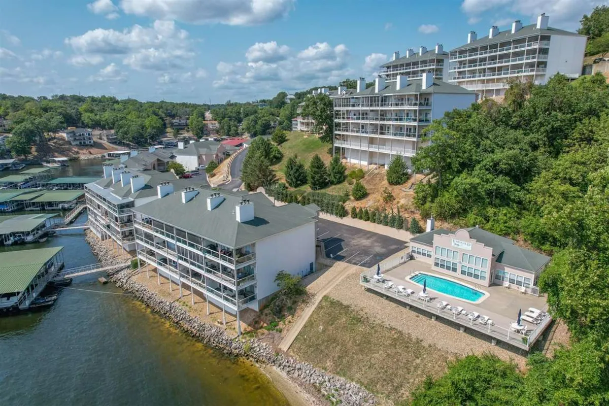 This lively scene features a pool set alongside the waterfront, framed by lush greenery and tasteful buildings. The pool area is active, with space for sunbathing and hosting barbecues, while the proximity to the water hints at easy access for boating or evening walks.