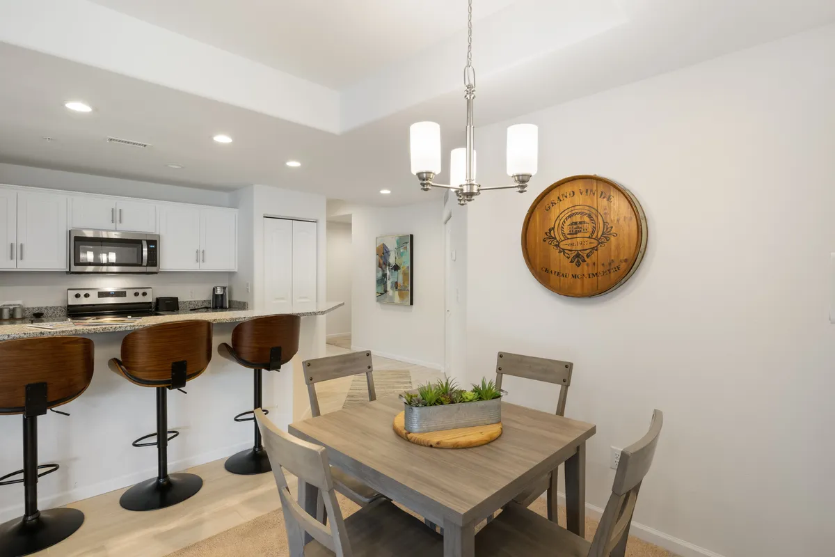 A cozy dining table is surrounded by bar stools, with eye-catching artwork and wooden accents on the wall, creating a welcoming ambiance for group dining and casual get-togethers.