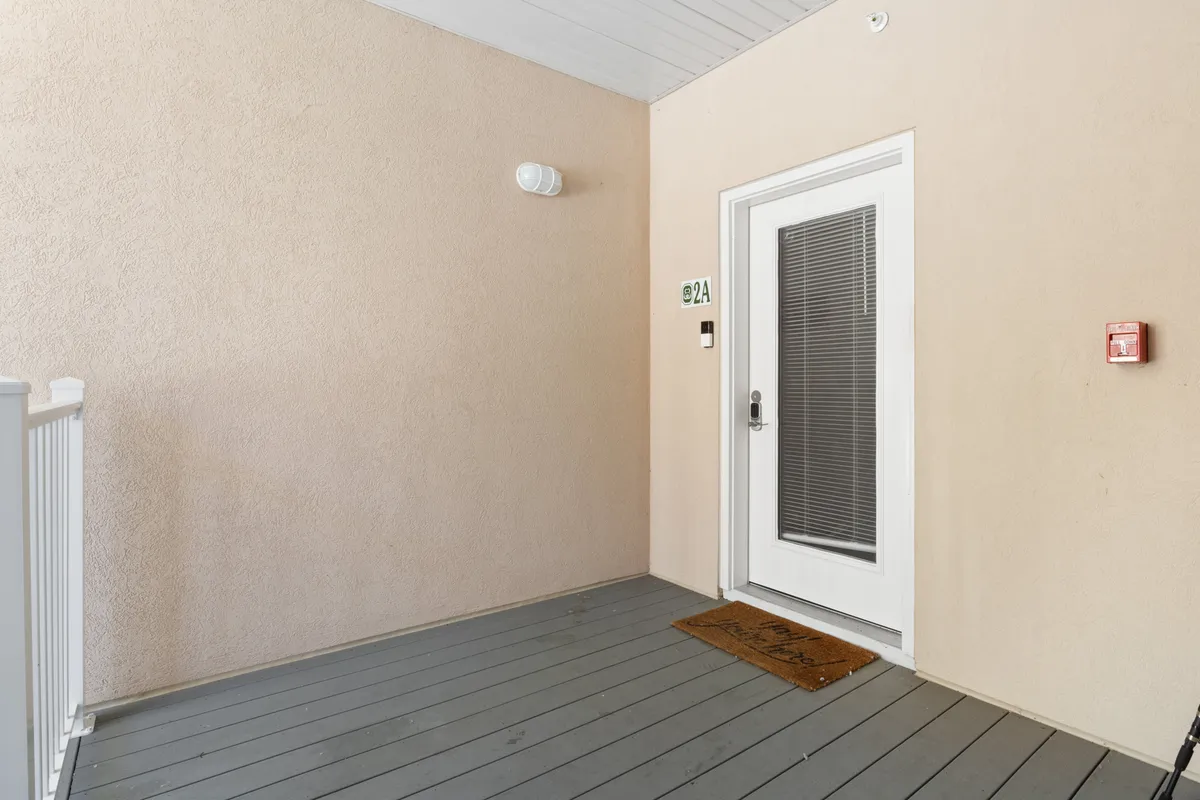 The image shows a welcoming front door with a doormat and house number sign, all set against a tidy entryway. The entry has only a couple of steps, making it accessible for guests with strollers or those with limited mobility. The exterior is inviting, hinting at the ease of access emphasized in the section.